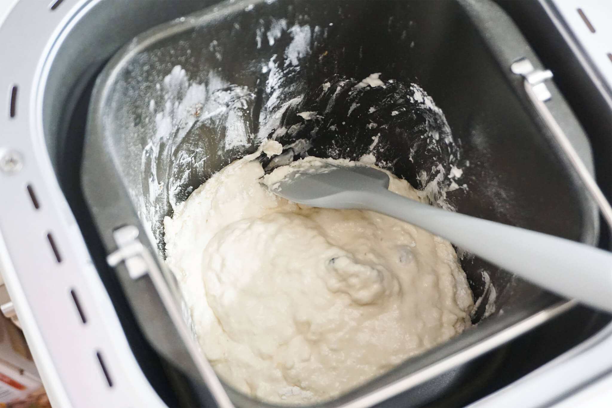 ホームベーカリーで高加水パンを作っている途中、ゴムベラでパンケース側面の粉を落としている様子