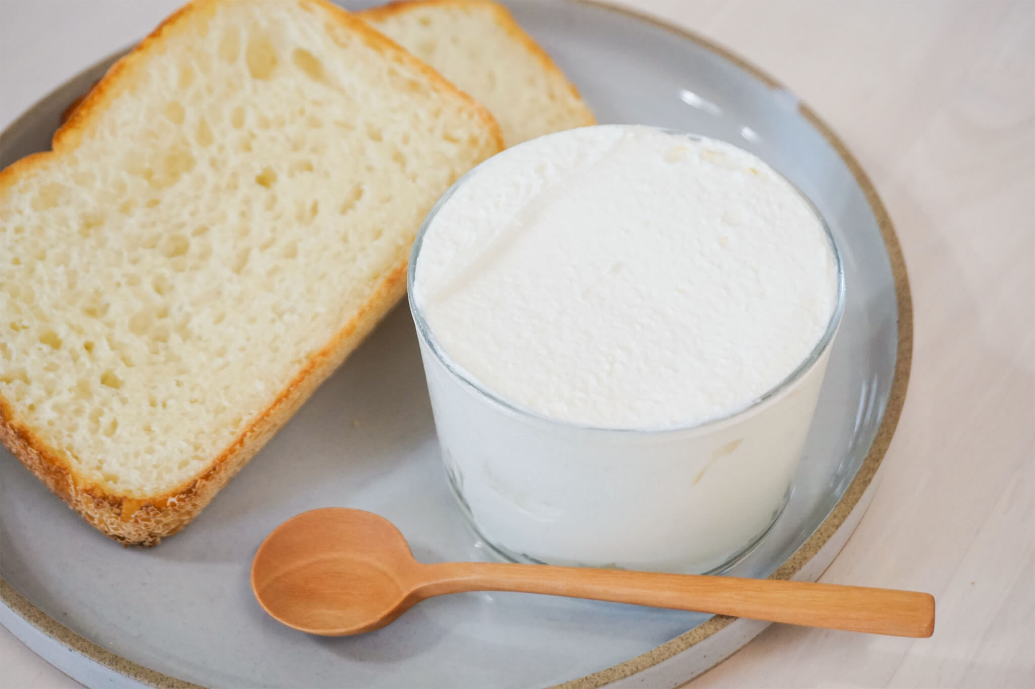 フレッシュチーズを入れた器をパンが盛られた皿にスプーンと共に添えた様子